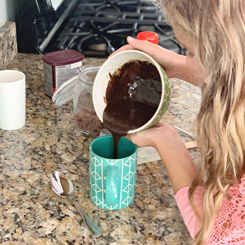 girl pouring chocolate cake batter into green mug