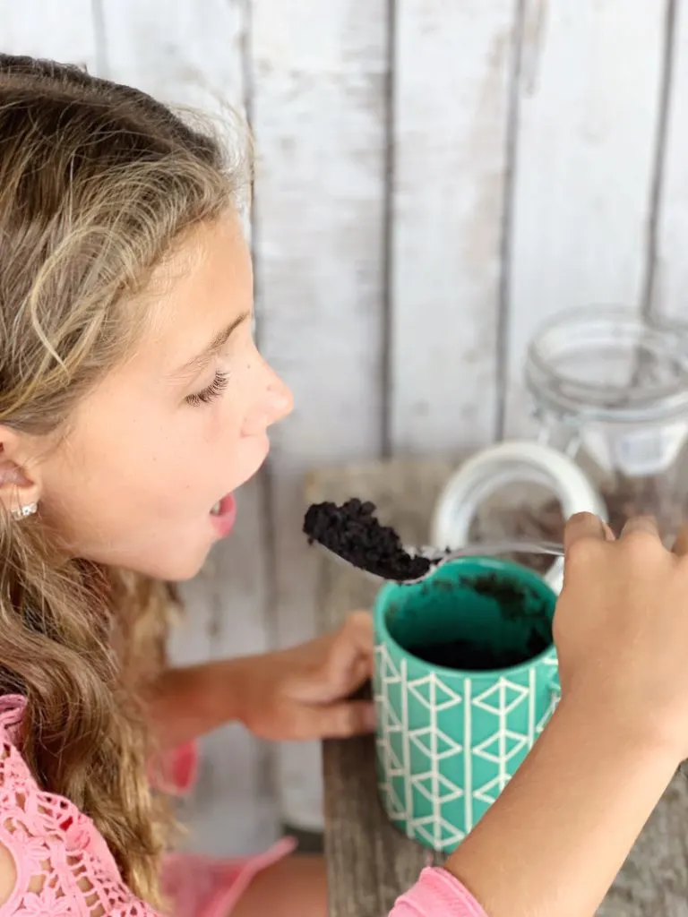 girl taking a bite of eggless chocolate mug cake out of a green mug