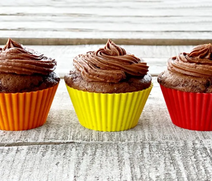 Three chocolate cupcakes lines up in a row with chocolate frosting.