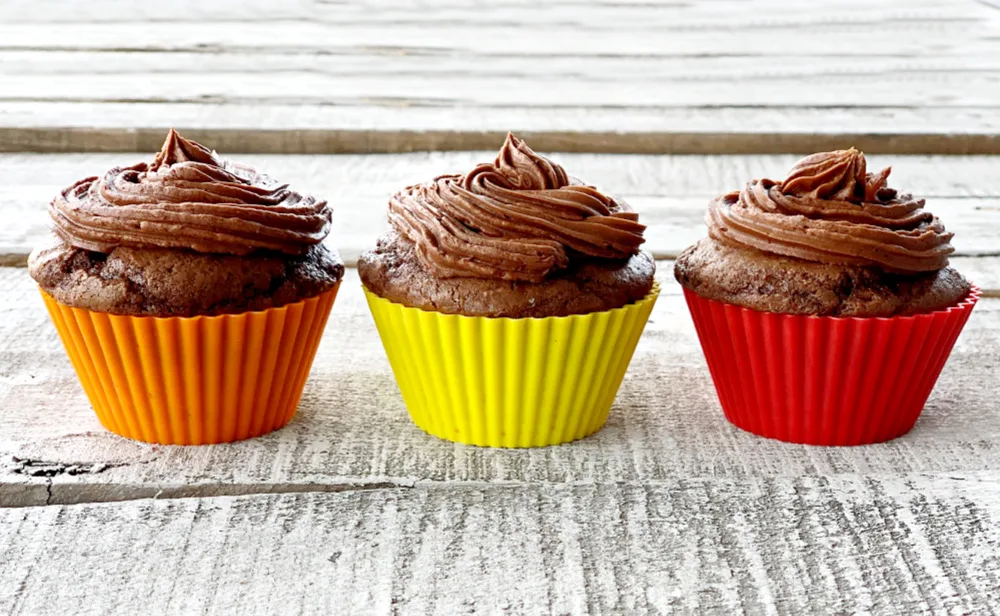 Three chocolate cupcakes lines up in a row with chocolate frosting.
