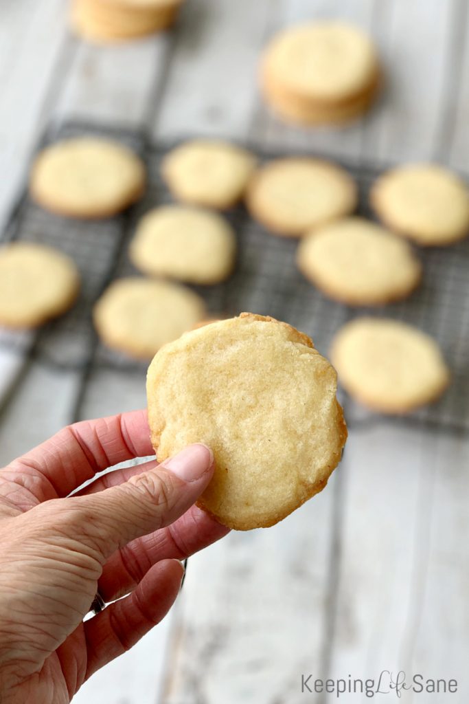 hand holding round eggless sugar cookie with black cooling rack in the background