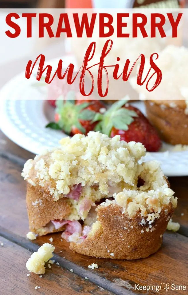 eggless strawberry muffins cracked open in front of a white plate with strawberries with more muffins.