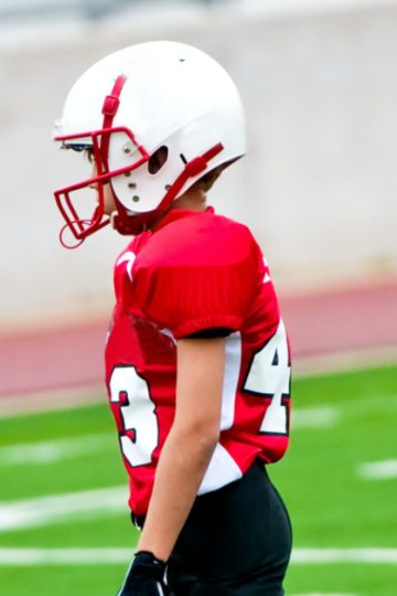 Boy in red football uniform standing on football field