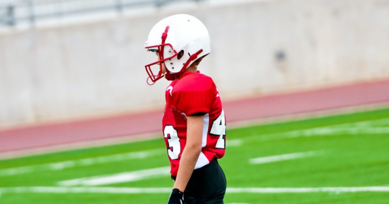 Boy in red football uniform standing on football field
