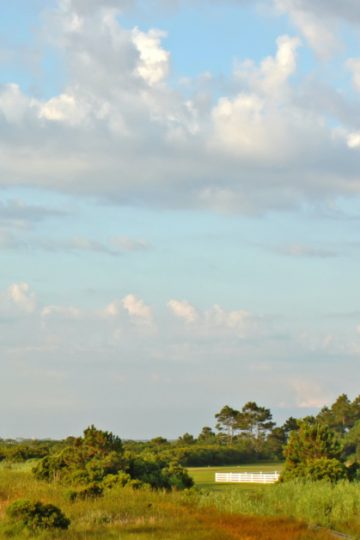 Walkway leading to the Bodie Island lighthouse over marshes of the Cape Hatteras National Seashore against white clouds and a blue morning sky