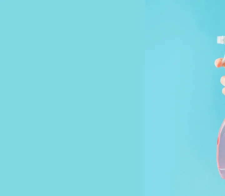 hand with pink spray bottle with blue background