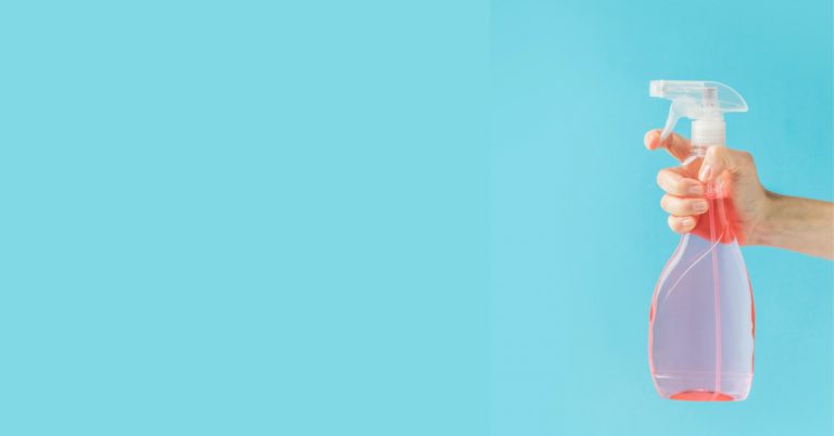 hand with pink spray bottle with blue background