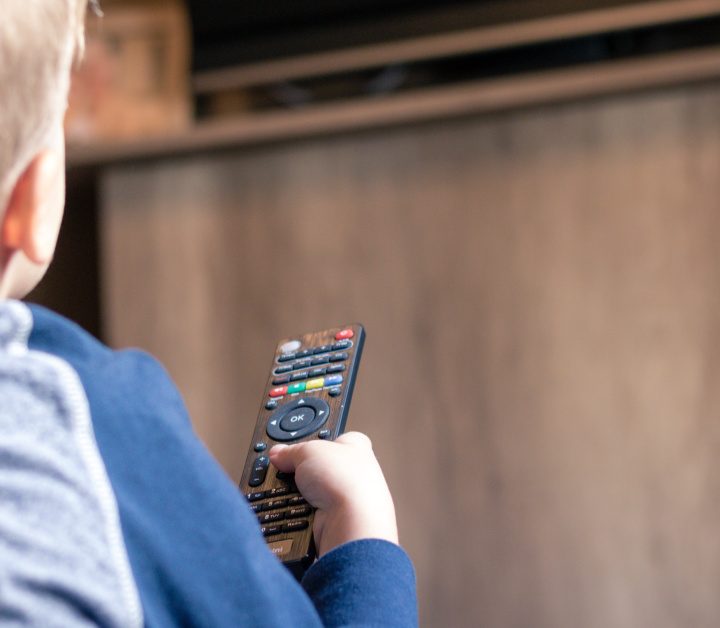 Kid watching TV and changing channels with remote control.