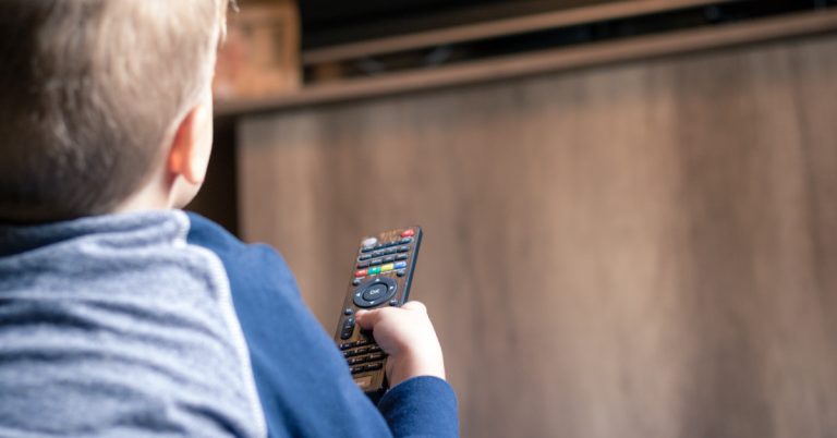 Kid watching TV and changing channels with remote control.