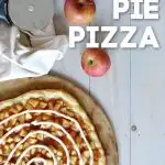 Overhead view of apple pie pizza with icing swirl with 2 red apples and pizza cutter