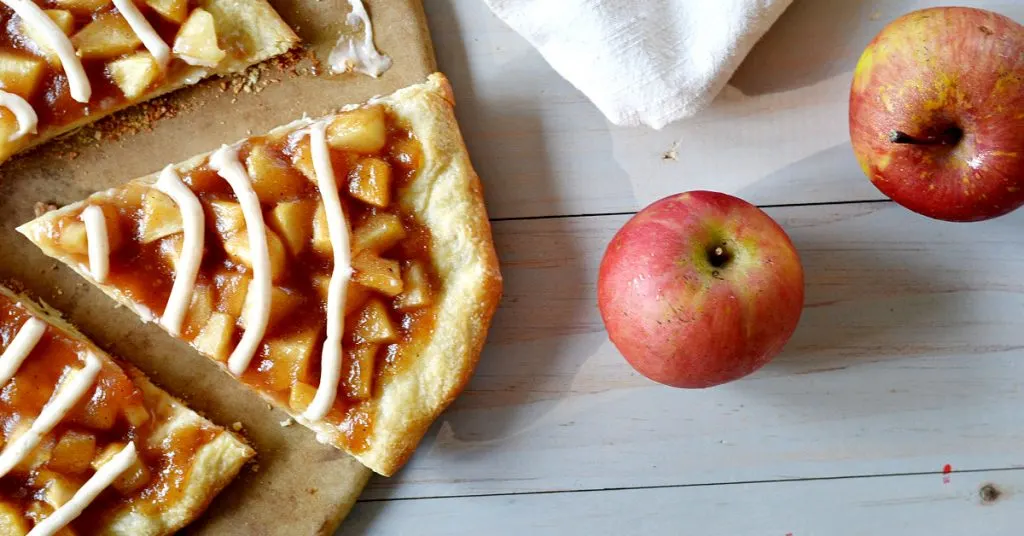 Slice of apple pie pizza with 2 red apples