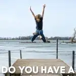 Kid in jeans jumping off dock into a lake.