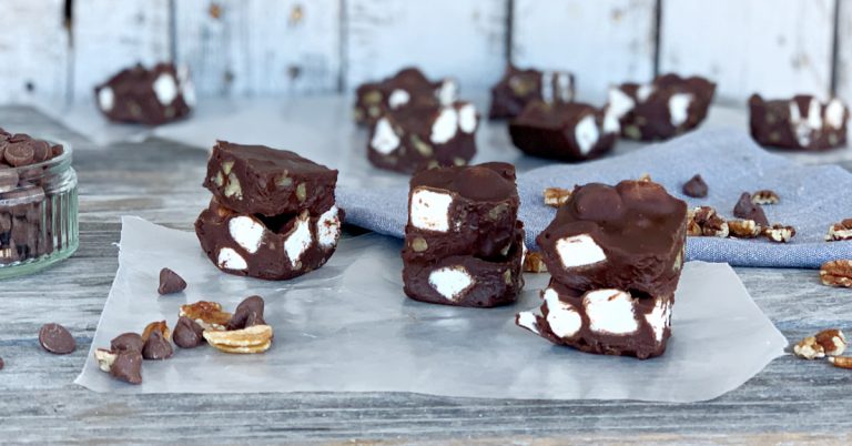 Lots of pieces of chocolate coffee fudge on wax paper with chocolate chips and pecans sprinkled around