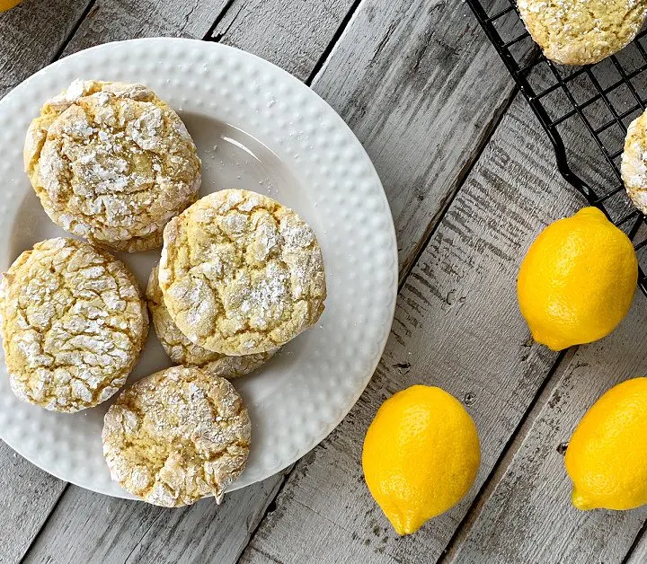 overhead view of white plate with lemon cookies with lemons on wooden table