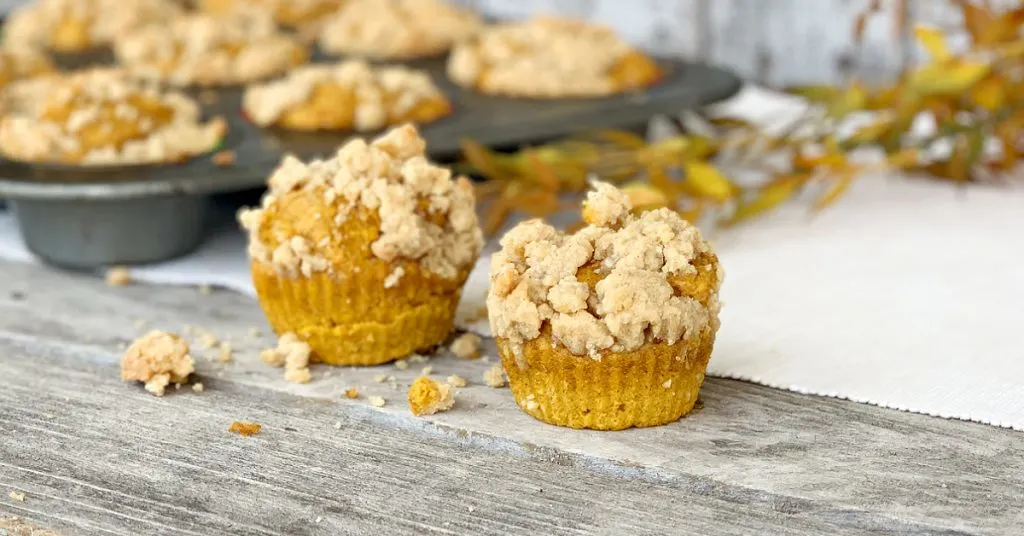 2 pumpkin muffins with muffin tin in background