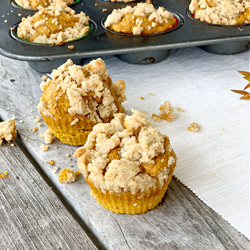 2 egg free pumpkin muffins with crumbles on top with muffin pan in background
