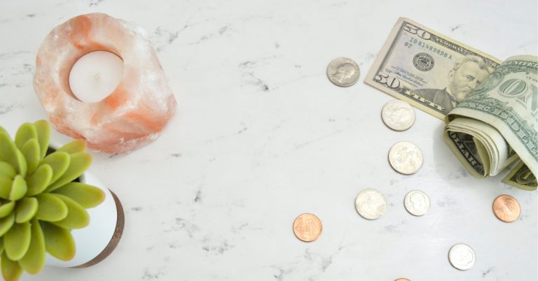 money sprinkled on white marble table toip with green plant and pink candle