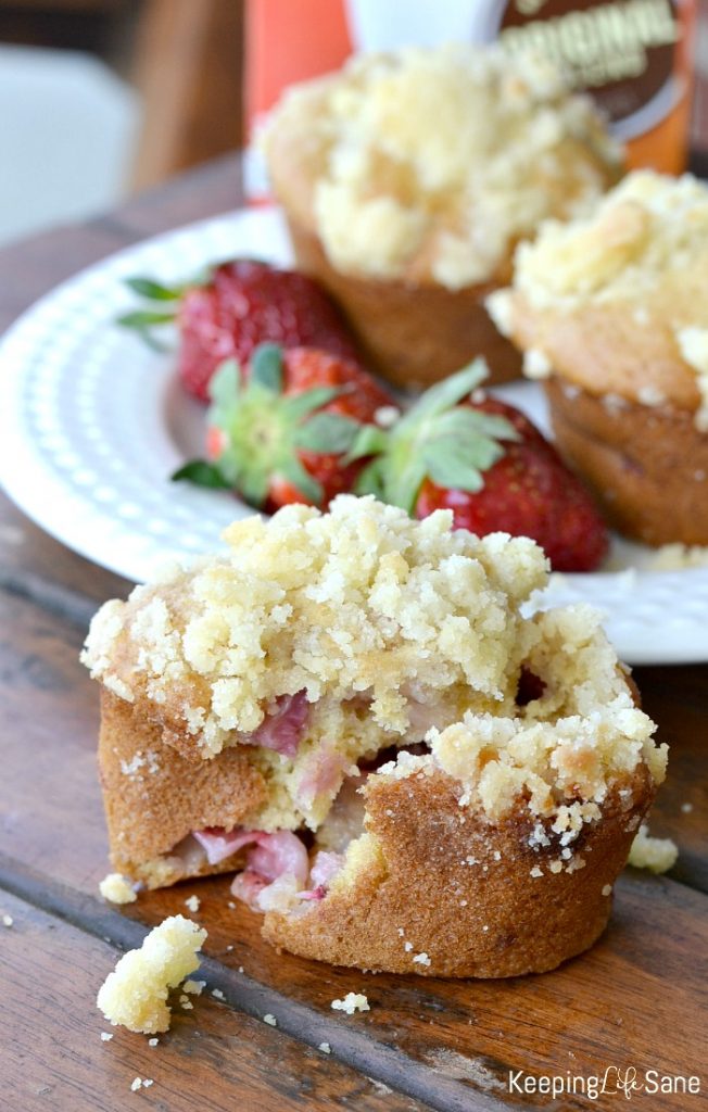 strawberry muffins cracked open in front of a white plate with strawberries with more muffins.