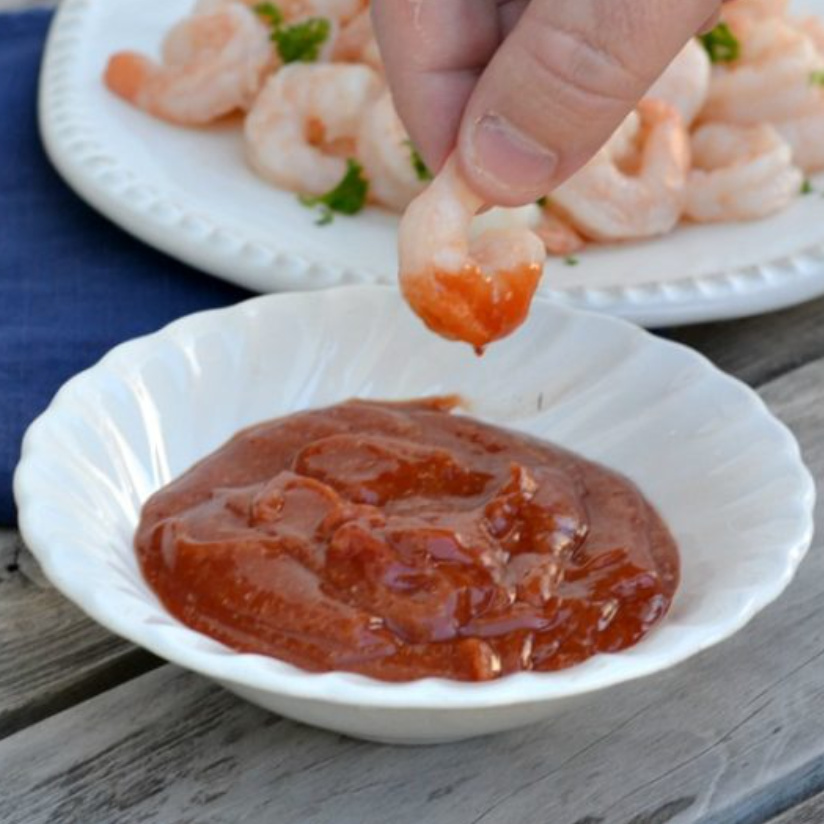white bowl with cocktail sauce and a hand that dipped a shrimp in