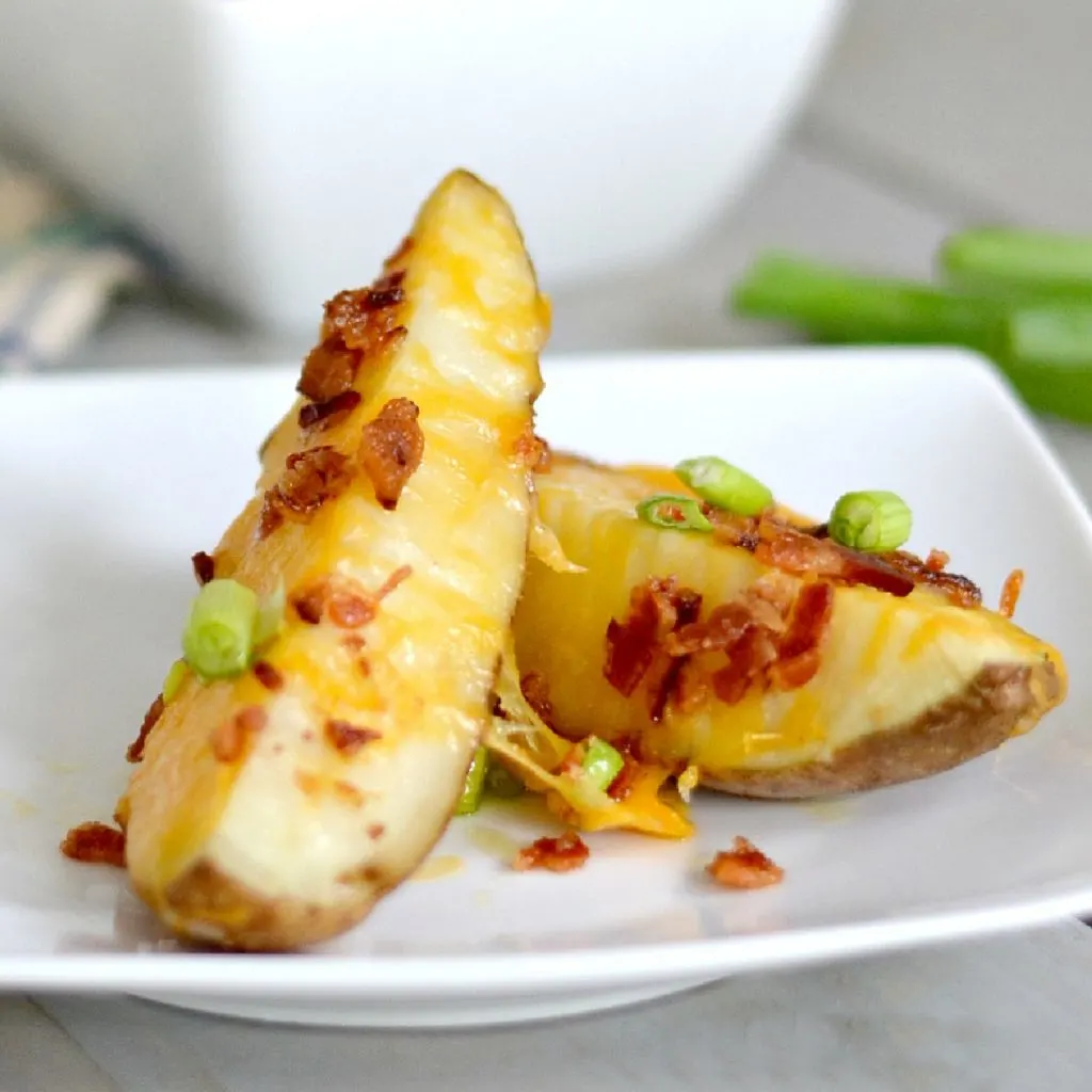 White square plate with 2 loaded potato wedges with cheese and bacon and a few green onions