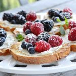 closeup view of berry bruschetta on round white platter- toast french bread with cream cheese spread with blueberries, blackberries and raspberries