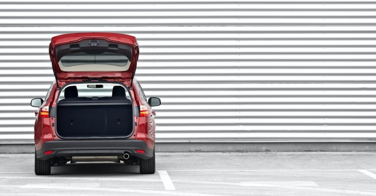 Red car with the truck open against white wall