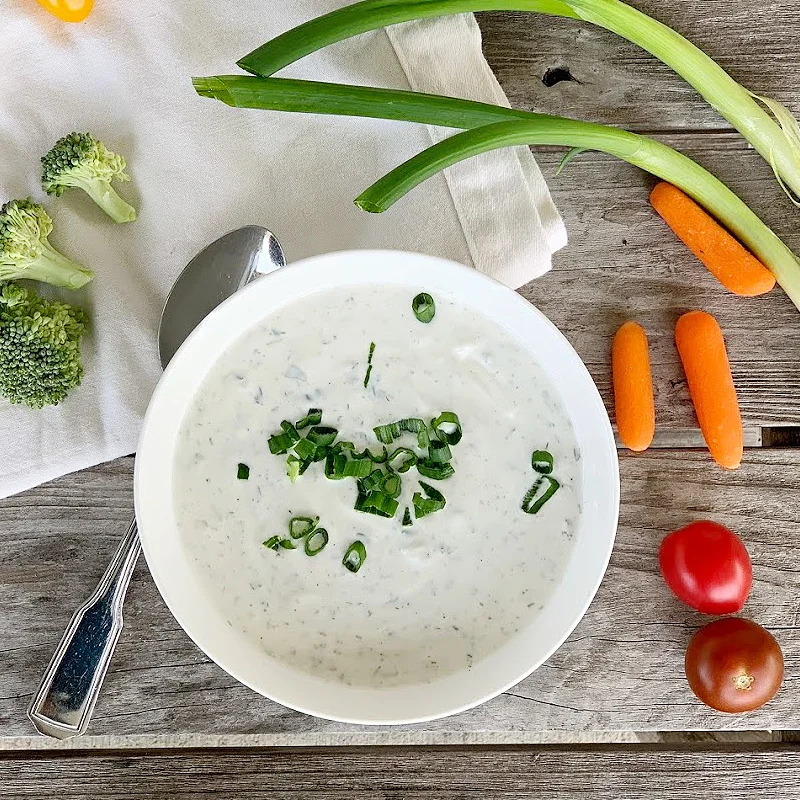 overhead view of ranch dip with scallions on top with cream napkin, green onions, carrots, cherry tomatoes, broccoli and a spoon