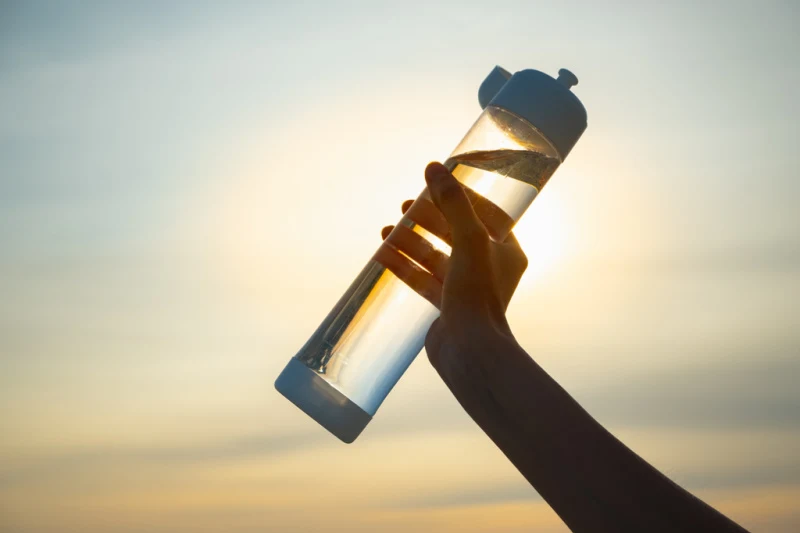Human hand holds a water bottle against the setting sun. Close up of a reusable water bottle in a human hand