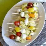 overhead view of white platter with a bunch of mini skewers of tortellini, grape tomatoes and mozzarella