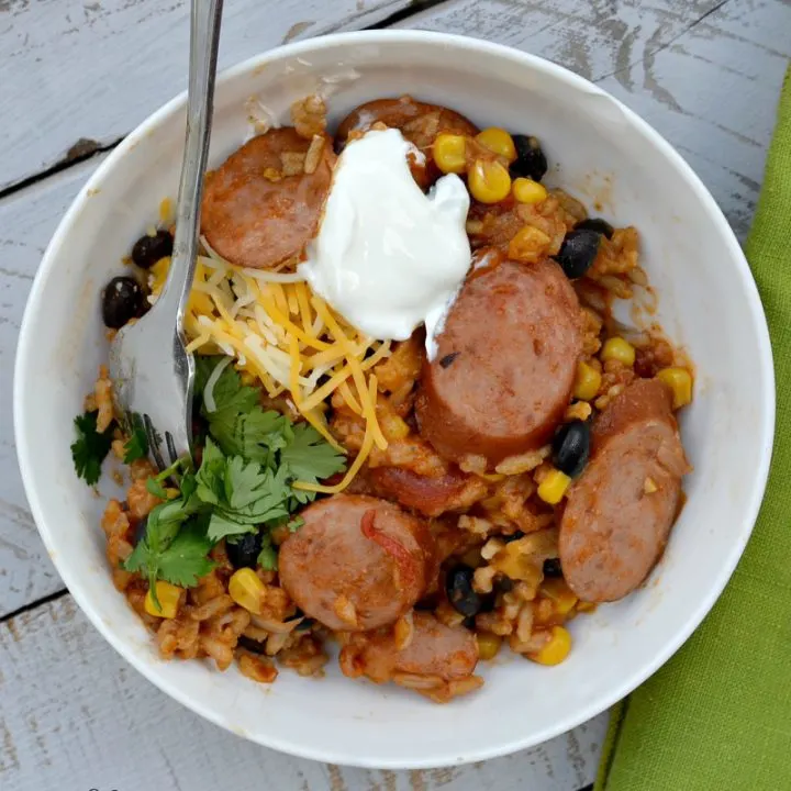 overhead view of mexican sausage casserole in white bowl with shredded cheese, sour cream and cilantro for garnish