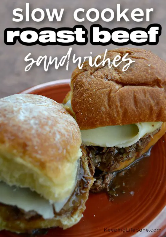 two slider roast beef sandwiches on dark red plate with meat adnd cheese and gravy dripping out.