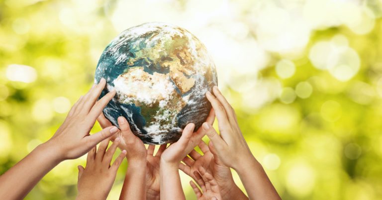 Group of children holding planet earth over defocused nature background with copy space