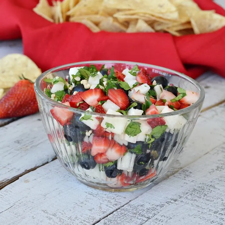 clear glass bowl with jicama salsa with strawberries and blueberries and cilantro