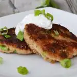 closeup of two tuna patties on a white plate with sour cream dill topping and chopped chives