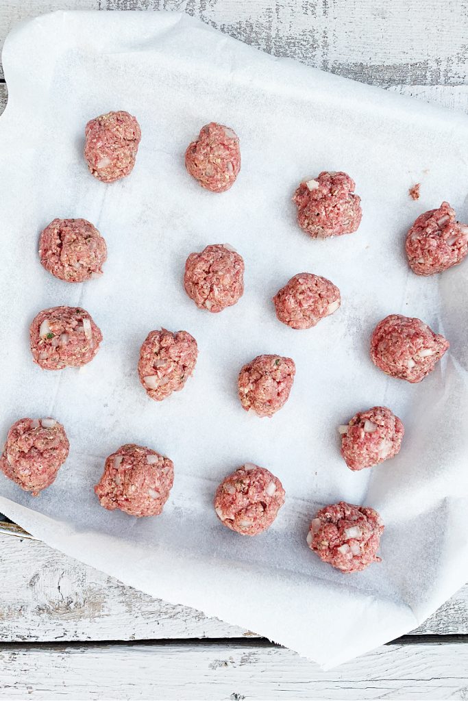 overhead shot with raw meatballs on baking pan lined with parchment paper