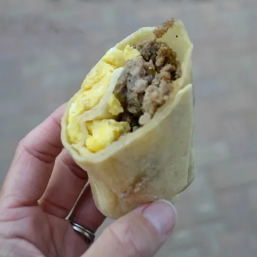 hand holding campfire burrito with eggs and ground sausage in tortilla