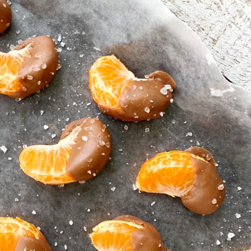 closeup overhead view of chocolate covered oranges with sea salt on parchment paper that's on cookie sheet
