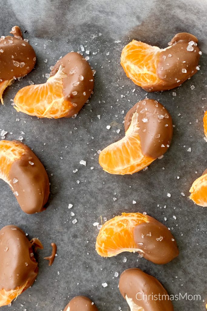 closeup overhead view of chocolate covered oranges with sea salt on parchment paper that's on cookie sheet