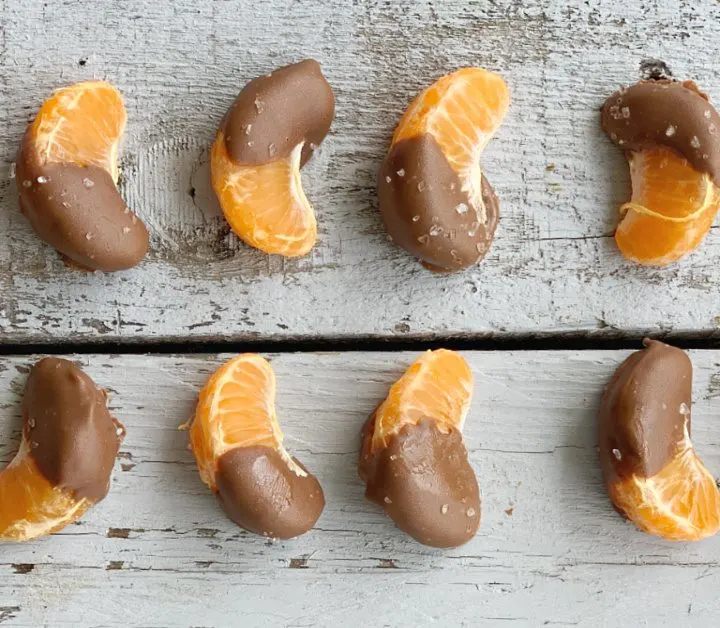 overhead view of two lines of chocolate dipped orange slices with sea salt on a grey wooden table