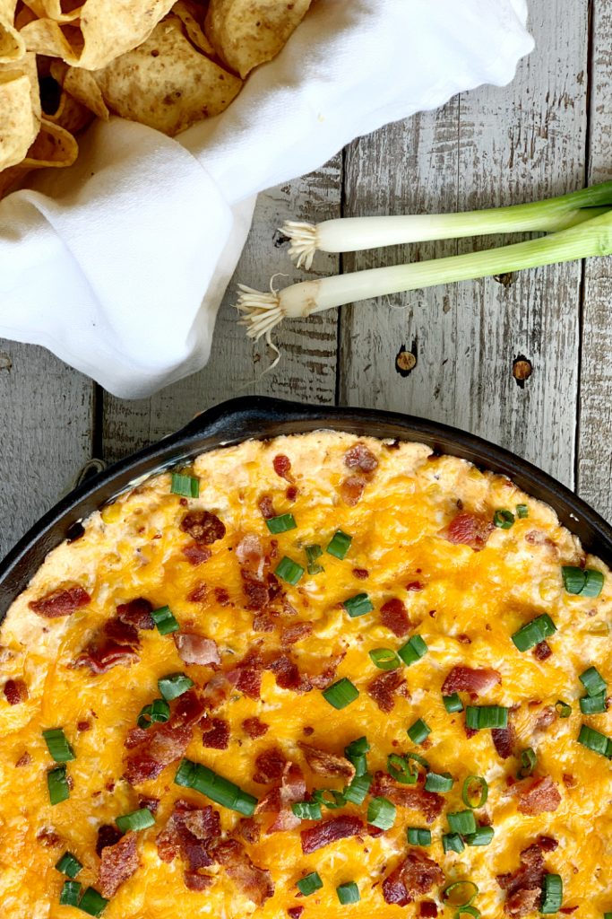 overhead view on cheesy corn dip with bacon and green onions in cast iron skillet