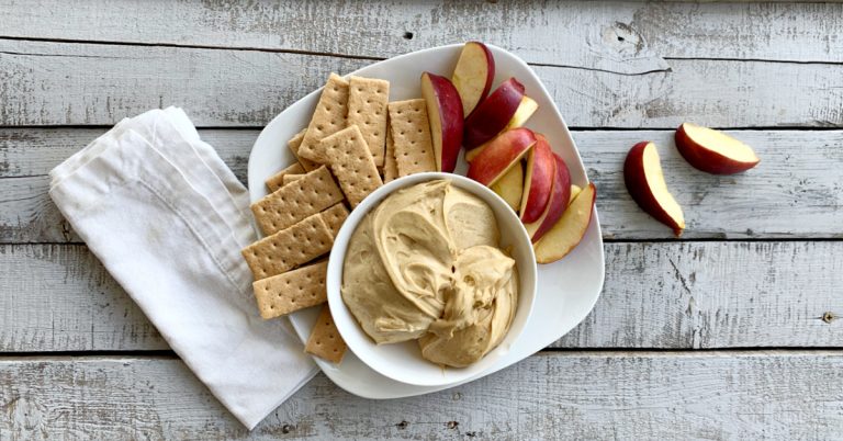 overhead view of gingerbread cheesecake dip with apples and graham crackers on white plate on wodden table