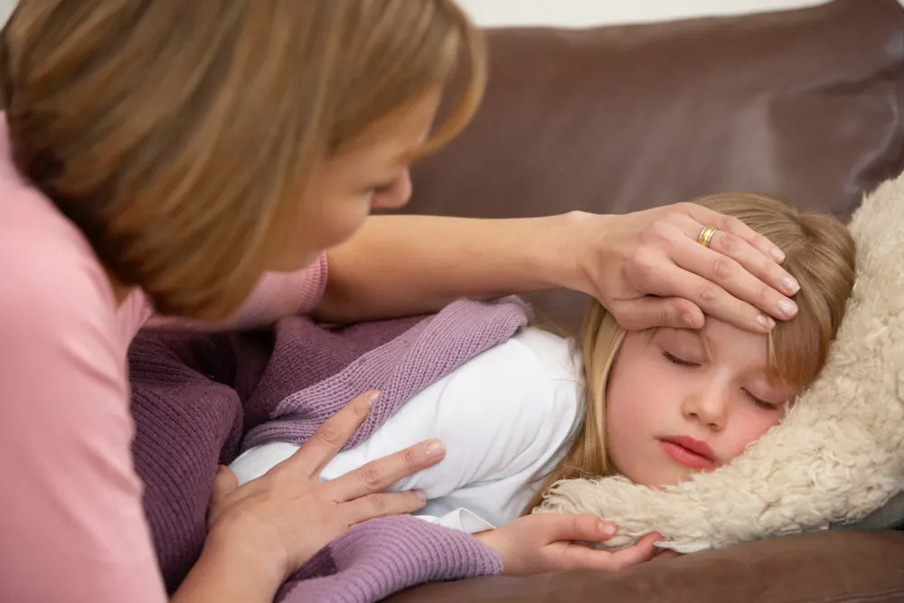 girl with stomach flu laying on couch while mom is feeling her head