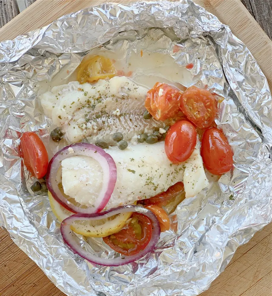 overhead view of Mediterranean Cod Recipe in foil with red onions and tomatoes on large cutting board