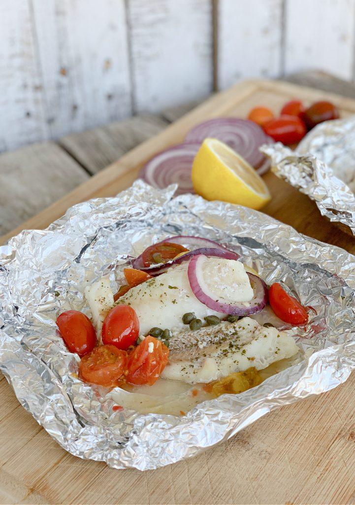 Mediterranean Baked Cod Recipe in foil with red onions and tomatoes on large cutting board
