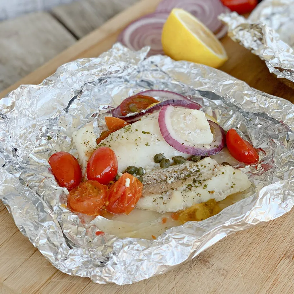 Mediterranean Cod Recipe in foil with red onions and tomatoes on large cutting board