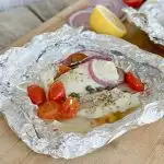 Mediterranean Cod Recipe in foil with red onions,and tomatoes on lare cutting board