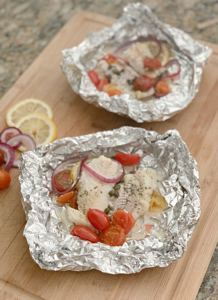Two Mediterranean Cod Recipe in foil with red onions and tomatoes on large cutting board