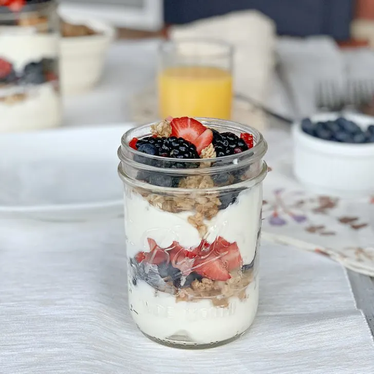 yogurt with granola and berries in a glass jar on a white tablecloth at a breakfast table