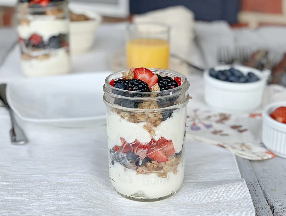 yogurt with granola and berries in a glass jar on a white tablecloth at a breakfast table