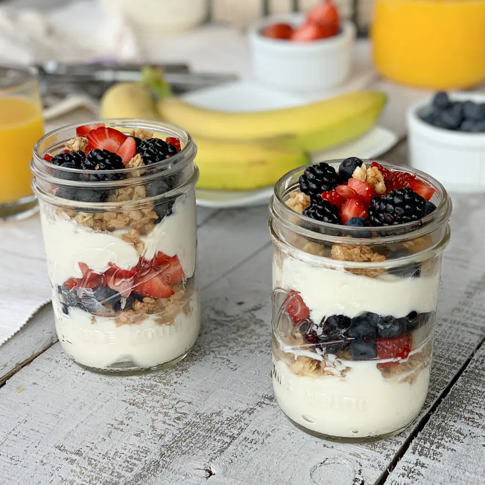 yogurt with granola and berries in glass jars on wooden table